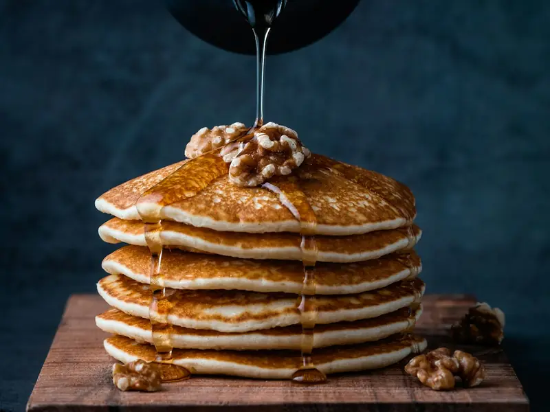 Tall stack of pancakes with syrup being poured over the top